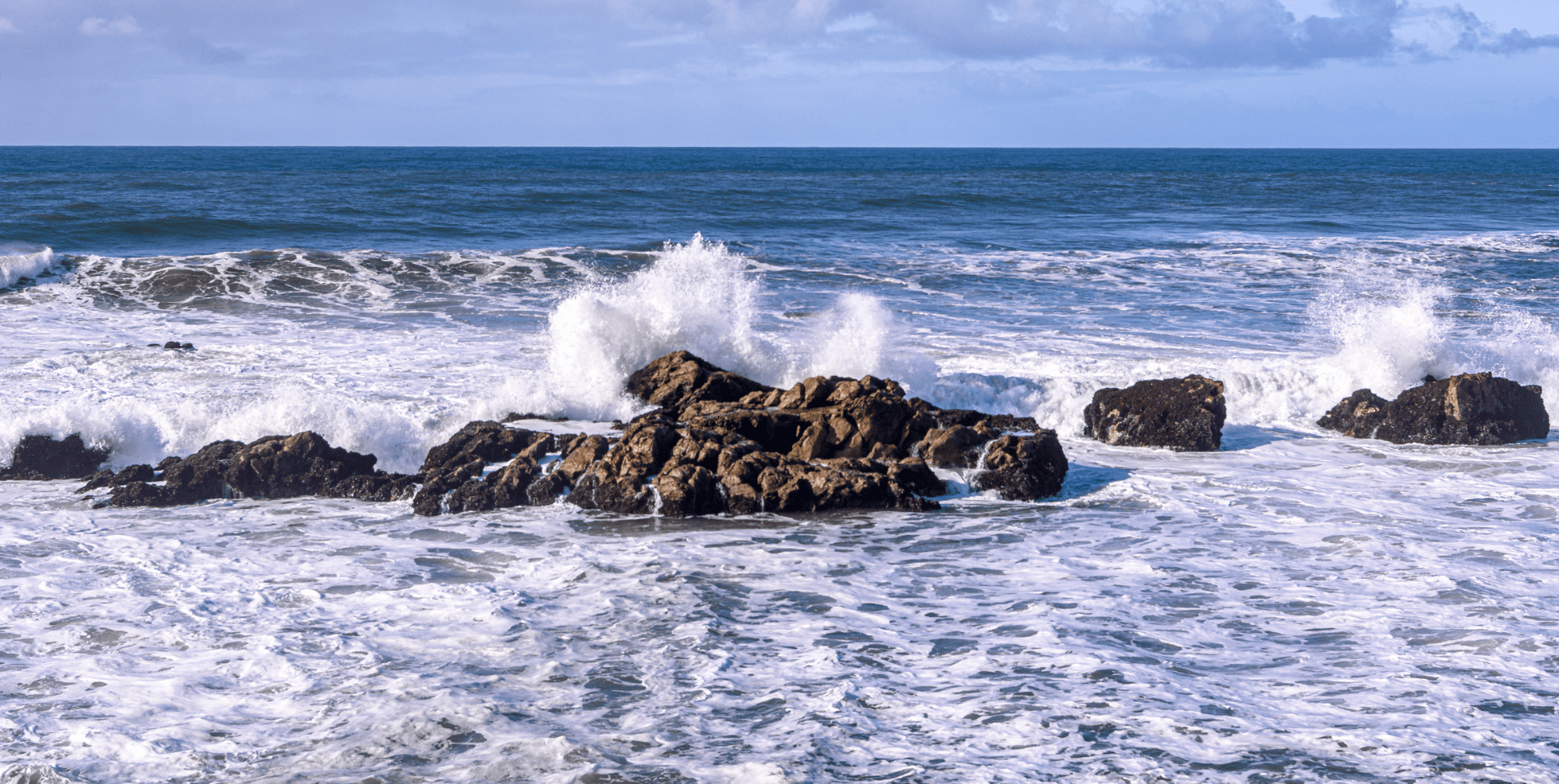 A rock formation in the ocean with waves crashing.